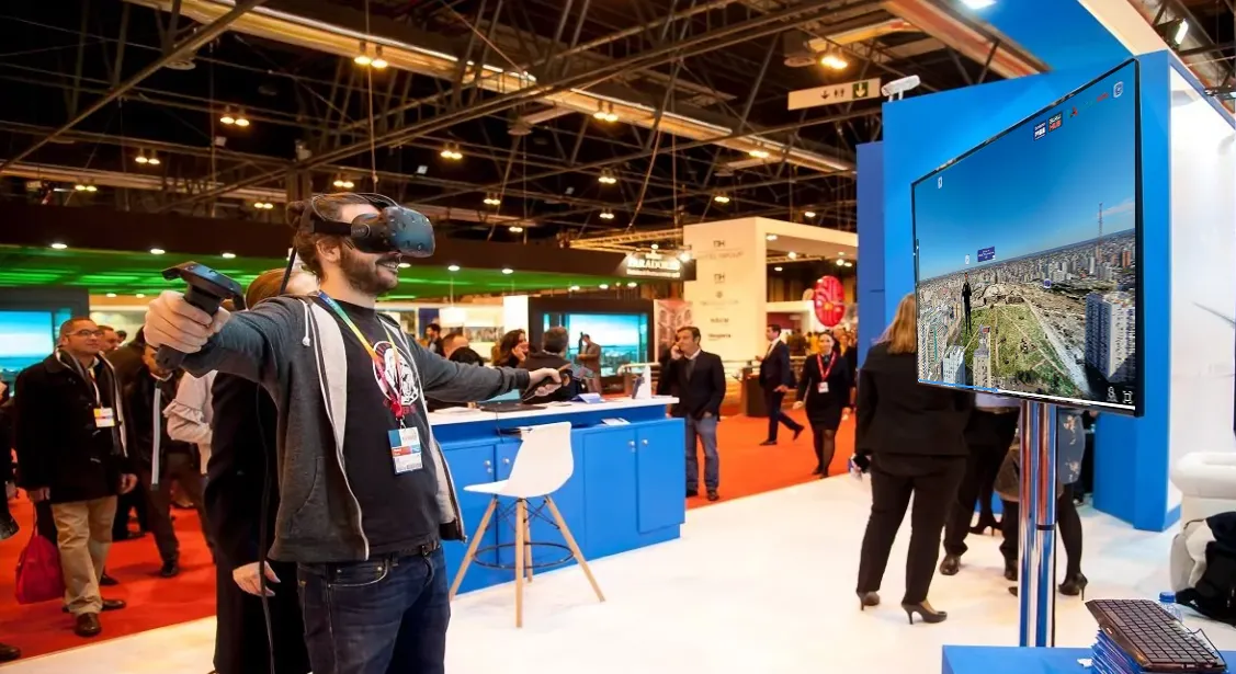 Un visitante con visor de realidad virtual en el stand de una feria, con el recorrido aéreo de Bahía Blanca en una pantalla.